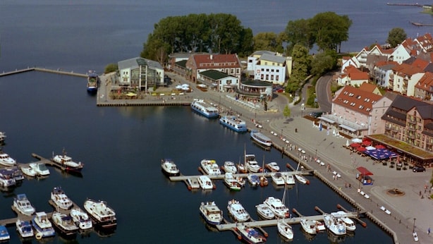 Un puerto deportivo con barcos amarrados, un paseo marítimo y edificios de arquitectura tradicional.