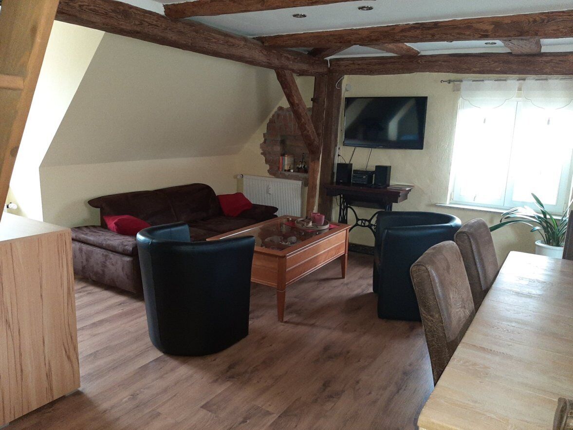 A cozy living room with a wooden ceiling, a sofa, a coffee table, and a TV mounted on the wall.