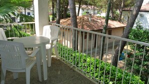 Un balcon agrémenté d’une table et de chaises, entouré de verdure et donnant sur un quartier résidentiel avec des maisons.