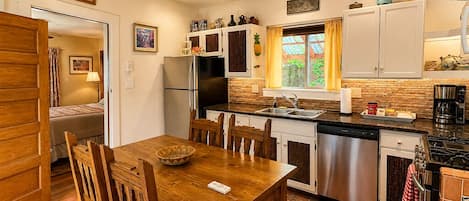 A compact kitchen with a dining table, chairs, a refrigerator, a dishwasher, and a stove.