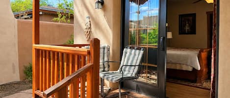 A wooden deck with a chair and a sliding glass door leading to a bedroom with a bed and a ceiling fan.