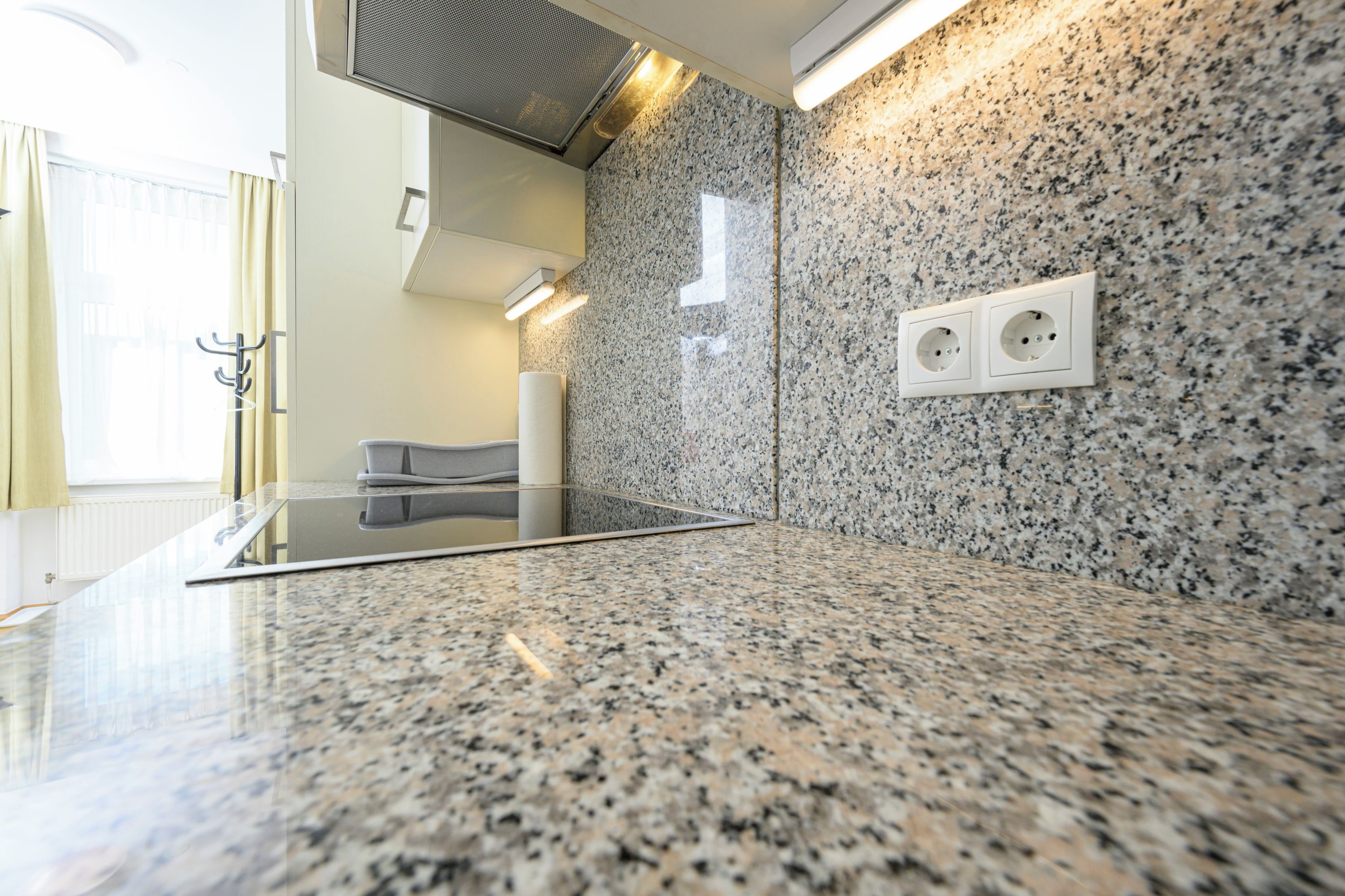 A modern kitchen with granite countertops, a built-in stove, and a wall-mounted power outlet.