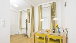 A dining area with a wooden table, yellow chairs, a bottle of wine, and a vase with flowers.