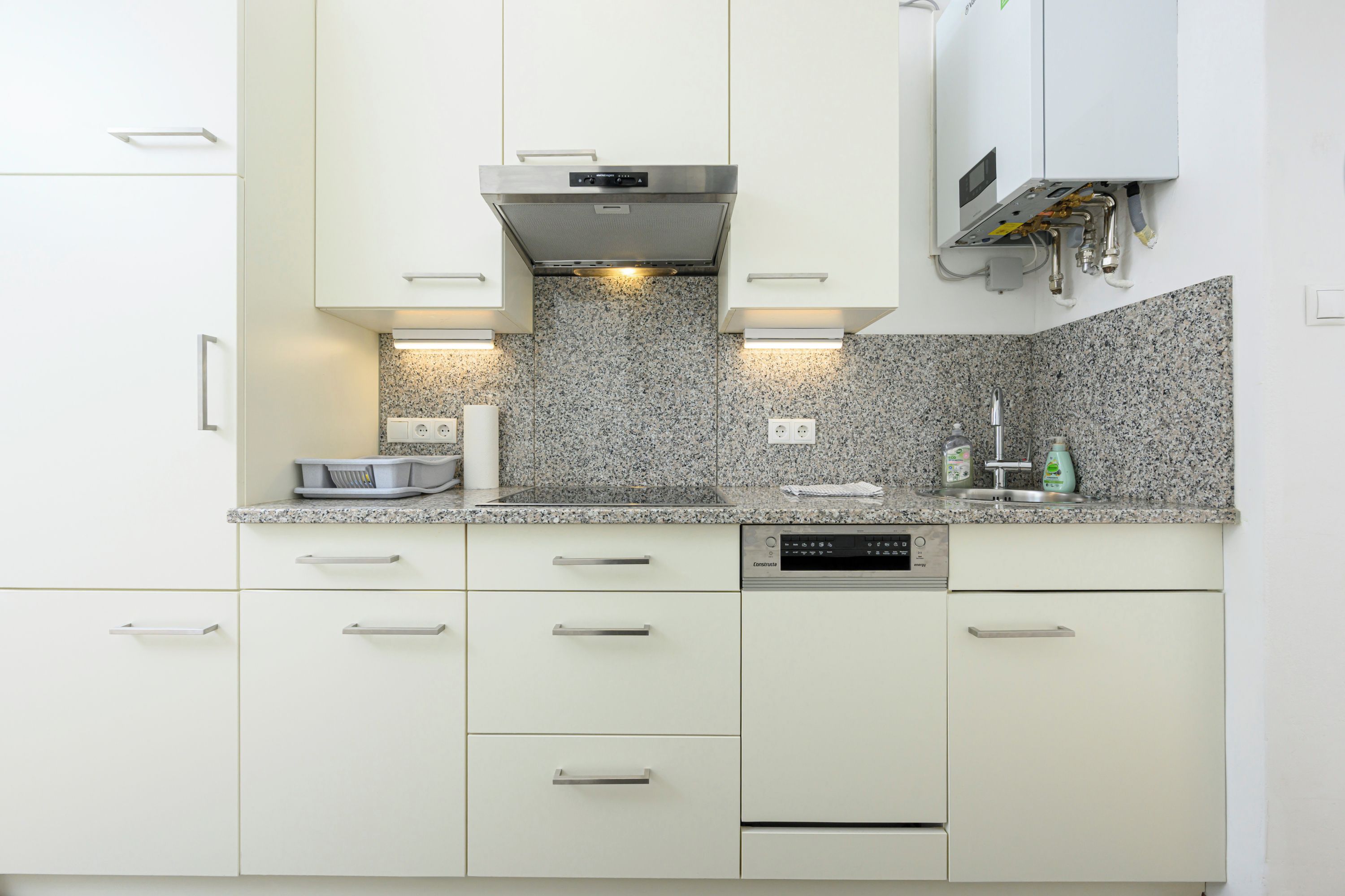A modern kitchen with white cabinetry, granite countertops, and built-in appliances including a dishwasher and a microwave.