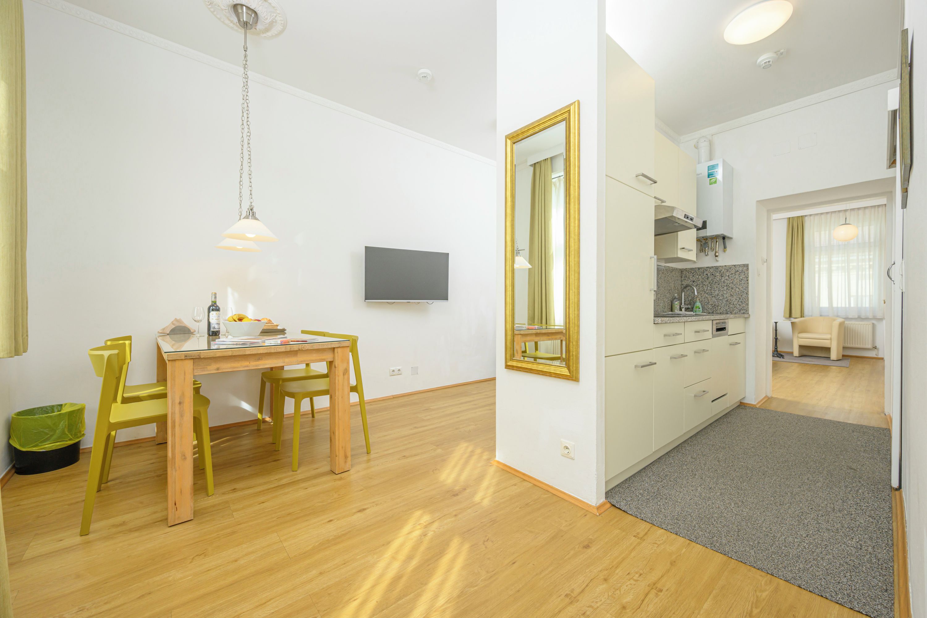 A modern kitchen with white cabinets, a large mirror, and a dining area with a wooden table and yellow chairs.