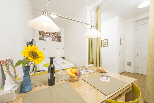Une chambre d’hôtel avec une table à manger dressée, agrémentée de verres à vin, d’un vase contenant un tournesol et d’un saladier rempli de fruits.