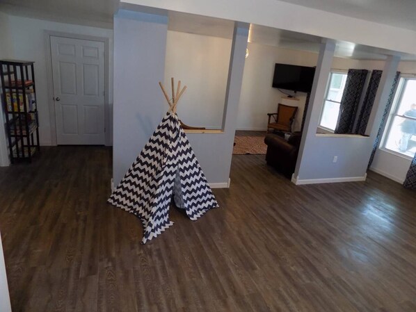 Un soggiorno con pavimento in legno, una porta bianca, un tenda tipica in bianco e nero a motivi a zig-zag e una televisione sullo sfondo.