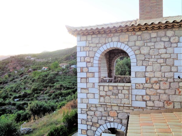 A stone building with a tiled roof, an arched window, and a small outdoor seating area.
