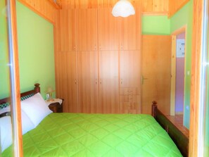 A bedroom with a large wooden wardrobe, a green bedspread, and a bedside table with a lamp.