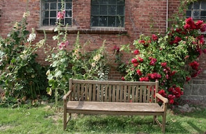A wooden bench in a garden with blooming flowers and a brick wall in the background.
