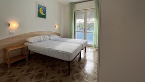 Une chambre à coucher avec un lit, une table de chevet, une lampe fixée au mur, un tableau et une fenêtre avec des rideaux.