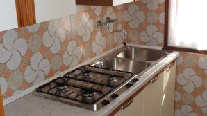 Une cuisine compacte dotée d’une cuisinière à gaz, d’un évier en acier inoxydable et d’un dosseret de carrelage à motifs.