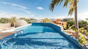 Una piscina con mosaicos azules, rodeada de palmeras y edificios.