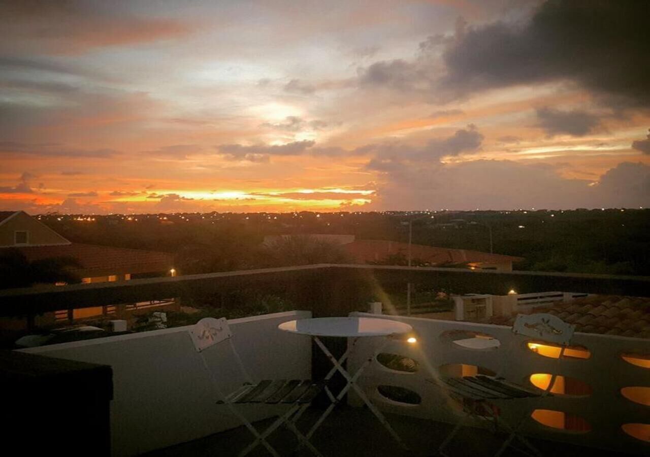 Une terrasse sur le toit, avec une table ronde et des chaises, d’où l’on peut admirer un coucher de soleil et les lumières de la ville au loin.