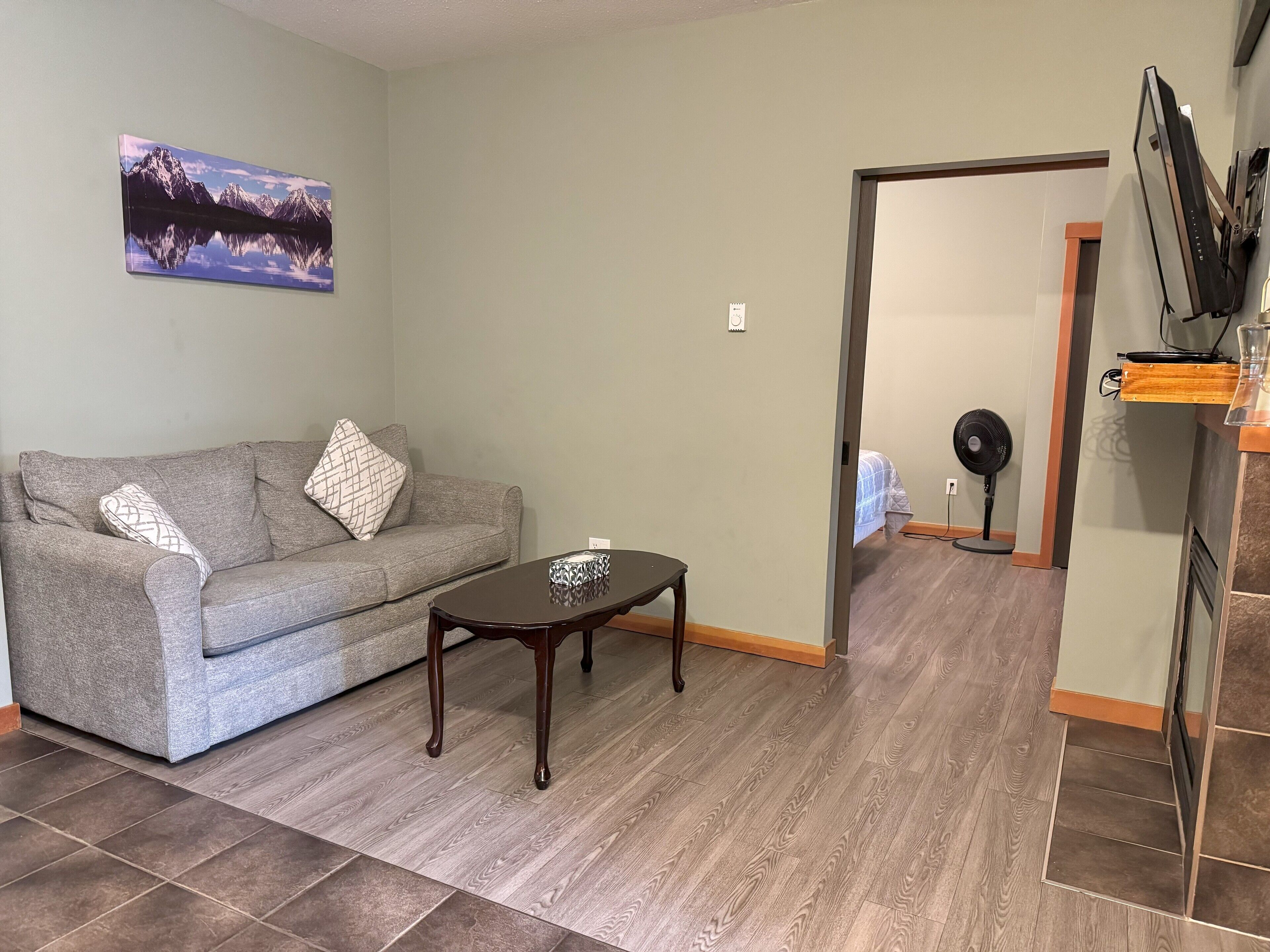 A living room with a grey sofa, a small wooden coffee table, and a painting of mountains on the wall.