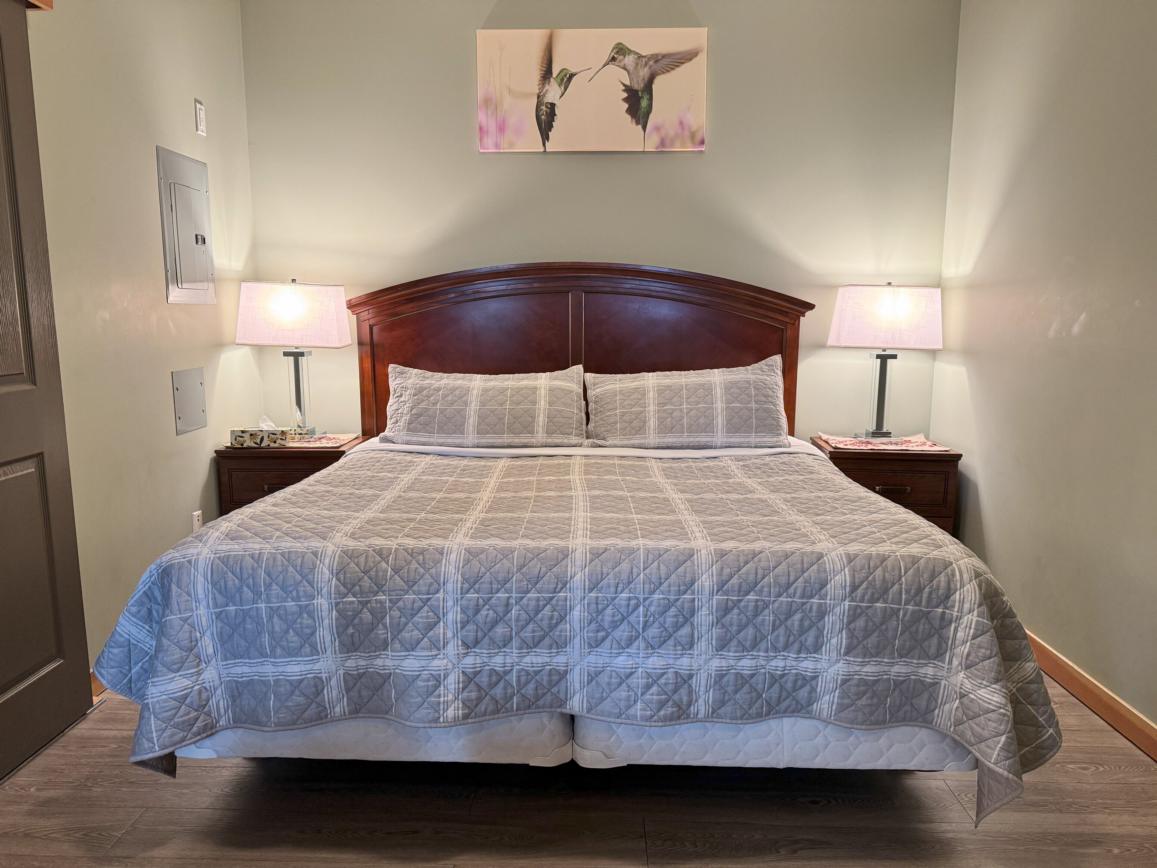 Una cama bien hecha con colcha acolchada, dos lámparas de noche y una obra de arte enmarcada sobre la cama.