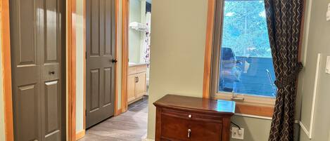 A hallway with wooden doors, a wooden dresser, and a window with patterned curtains.