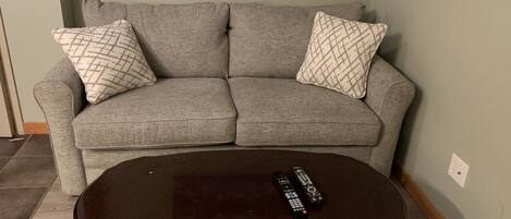A grey sofa with patterned cushions, a dark wooden coffee table, and a light green wall.