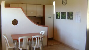 A compact kitchen with a dining area, white chairs, a wooden table, and a clock on the wall. - Villa Flavia, holiday home in Noto (Noto)