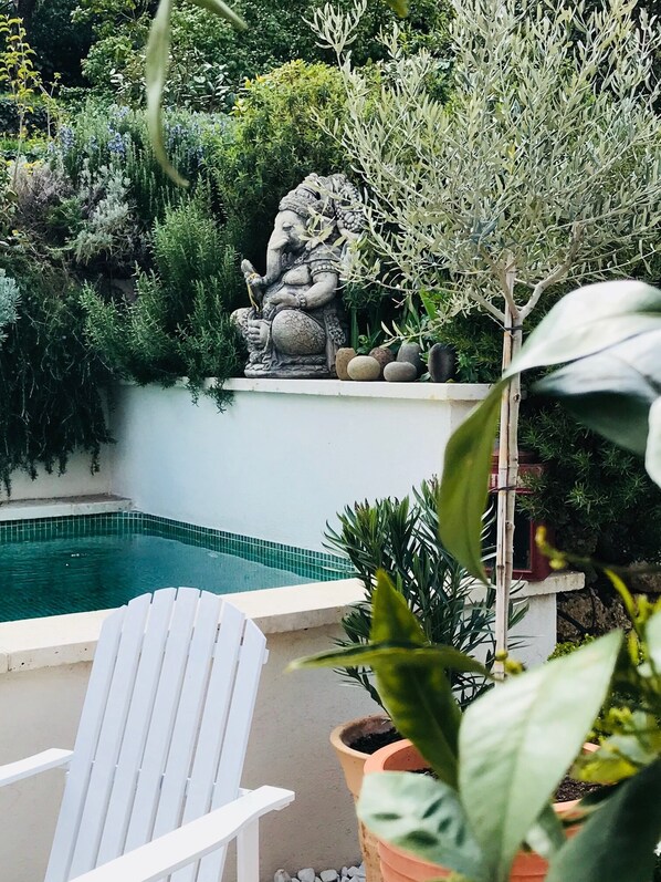 A pool area with a white chair, potted plants, and a stone statue.