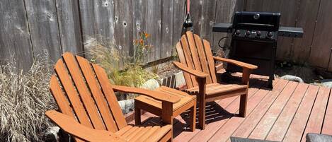 A wooden deck with two Adirondack chairs, a grill, and a dog waste station.
