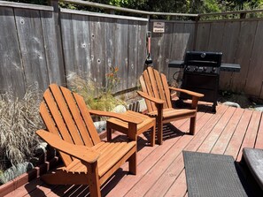 Une terrasse en bois avec deux fauteuils Adirondack, un barbecue et un espace dédié à la collecte des excréments canins.