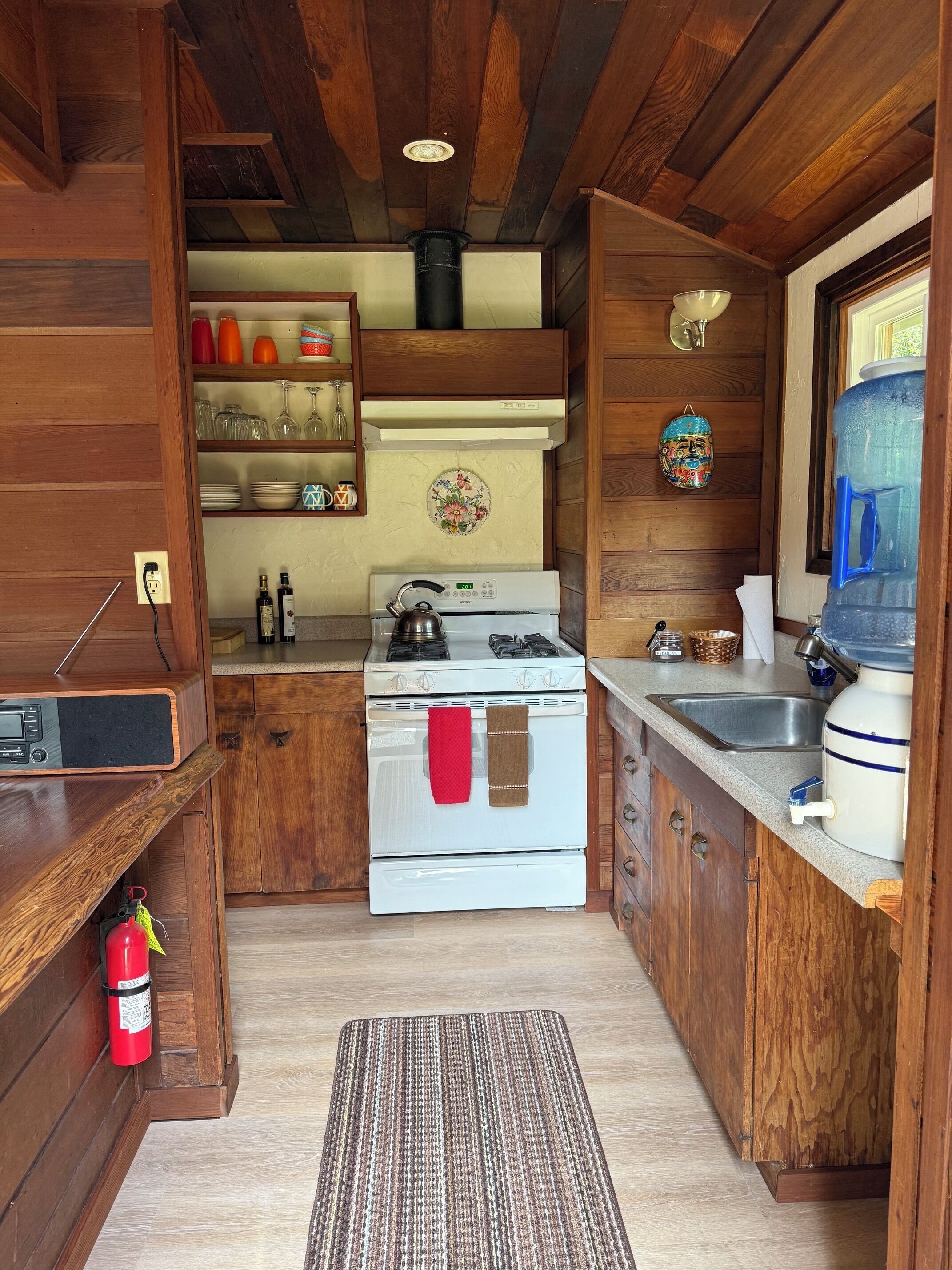 Una cocina compacta con armarios de madera, estufa, fregadero y dispensador de agua.