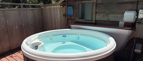 A hot tub on a wooden deck with a wooden fence in the background.