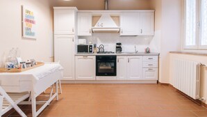 A kitchen with white cabinets, a microwave, a stove, and a coffee maker. There is a table with a tray of items and a picture on the wall. - Il Borgo degli Agrumi - Il Mandarino (Uzzano)