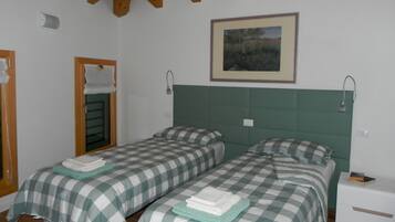 Una habitación con dos camas, cada una con ropa de cama y almohadas a cuadros, un cabecero verde, un cuadro enmarcado en la pared y una mesita de noche con un libro.
