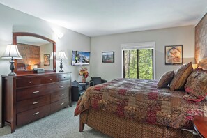 A bedroom with a large bed, a dresser, a mirror, and a window with a view of trees.