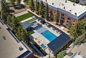 An aerial view of a residential area with a swimming pool, outdoor seating, and a building with a flat roof.
