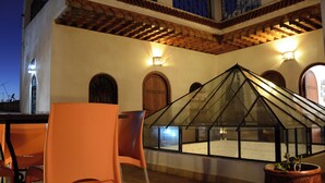 Eine Terrasse mit orangefarbenen Stühlen, einer Glaskonstruktion wie ein Gewächshaus und einer gefliesterten Decke.
