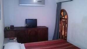 Ein Zimmer mit einem Bett, einem Fernseher auf einer Holzkommode, einer Tür mit Fenster und einer Klimaanlage an der Wand.