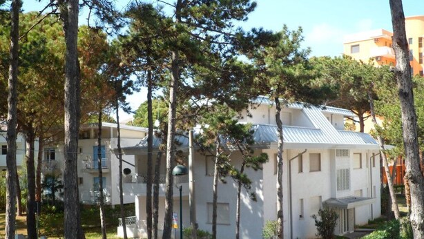 Ein Wohngebäude mit weißer Fassade, mehreren Balkonen und einem Metall-Dach.