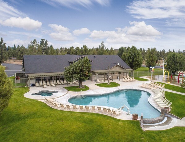 A large swimming pool with a curved design, surrounded by a grassy area and a covered pavilion with seating. - Awesome summers and gorgeous winters! (Redmond)