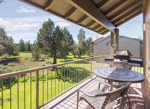 A balcony with a view of a grassy area and trees, a barbecue grill, and a round table with a metal chair. - Awesome summers and gorgeous winters! (Redmond)
