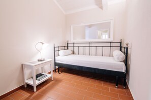 A small, neatly arranged bedroom with a single bed, a bedside table, and a mirror above the bed.