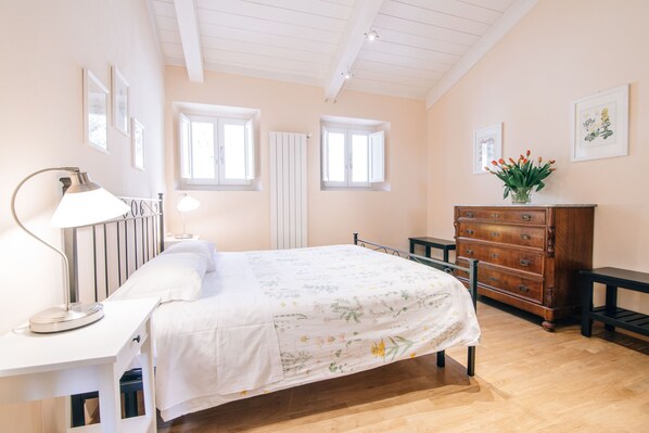 A bedroom with a bed, bedside table, lamp, dresser, and artwork on the walls.