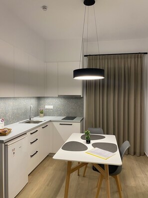 Une cuisine moderne avec un coin repas, comprenant une table agrémentée d’une plante, un luminaire suspendu et une vue sur l’extérieur grâce à une fenêtre avec des rideaux.