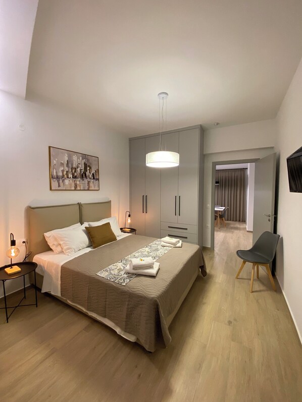 A modern bedroom with a bed, bedside lamps, a wardrobe, and a dining area in the background. - Economic Studio B1 (Iraklion Crete)