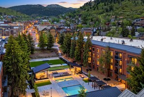 A hotel with a swimming pool, outdoor seating, and a view of the surrounding town and hills.