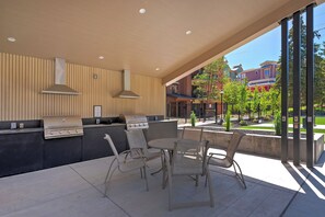 An outdoor patio with a grill, chairs, and a view of buildings.
