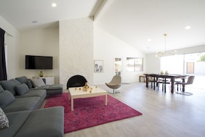 Una sala moderna con un sofá seccional gris, una mesa de centro y una chimenea. Hay un comedor con mesa y sillas.