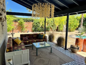 Un patio al aire libre con un sofá, una mesa de vidrio y una lámpara colgante.