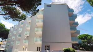 A multi-story residential building with balconies, parked cars, and a clear sky.