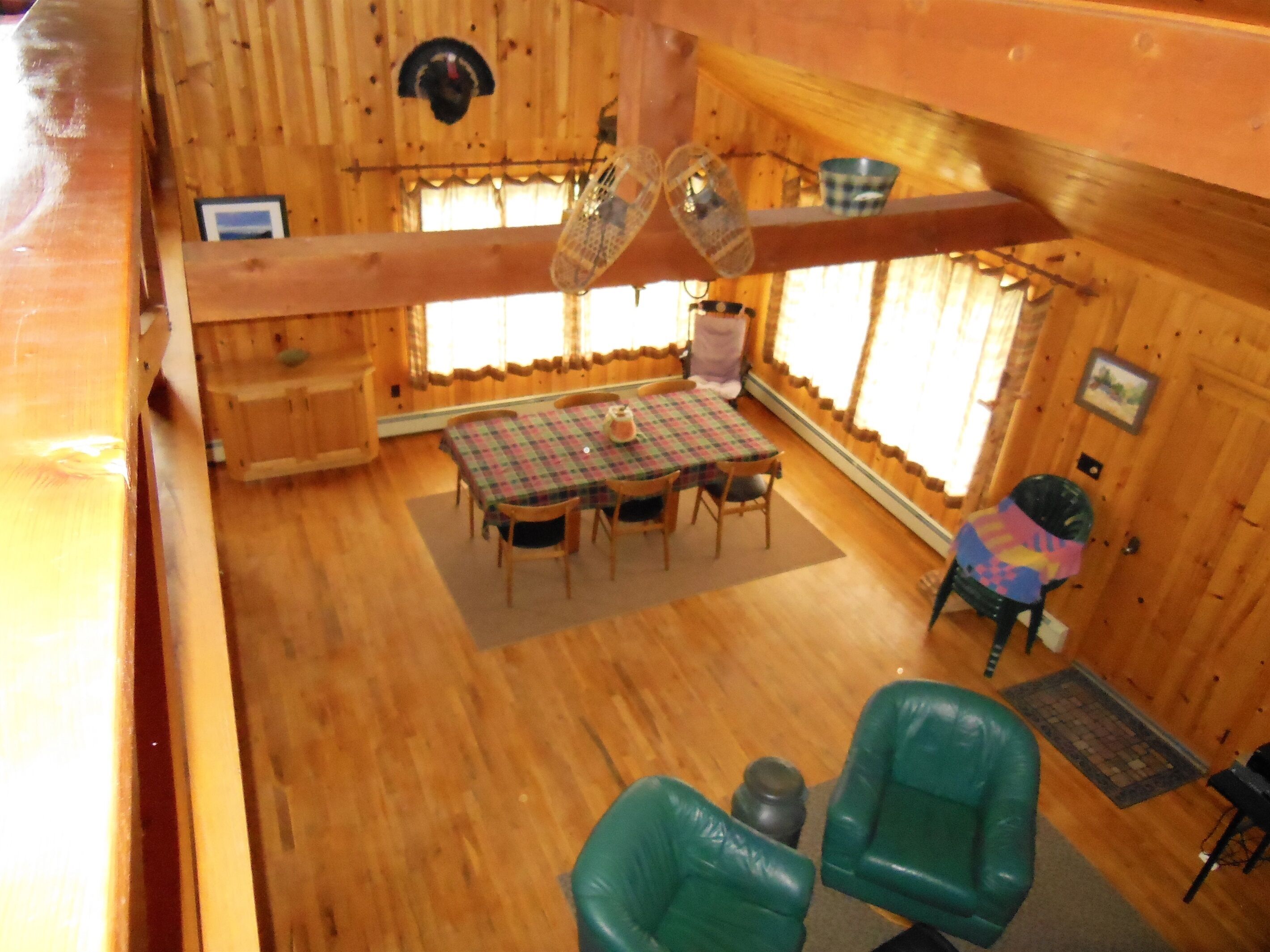 Interior d'una cabana de fusta amb una taula de dinar, cadires, una llar de foc i una finestra amb cortines.