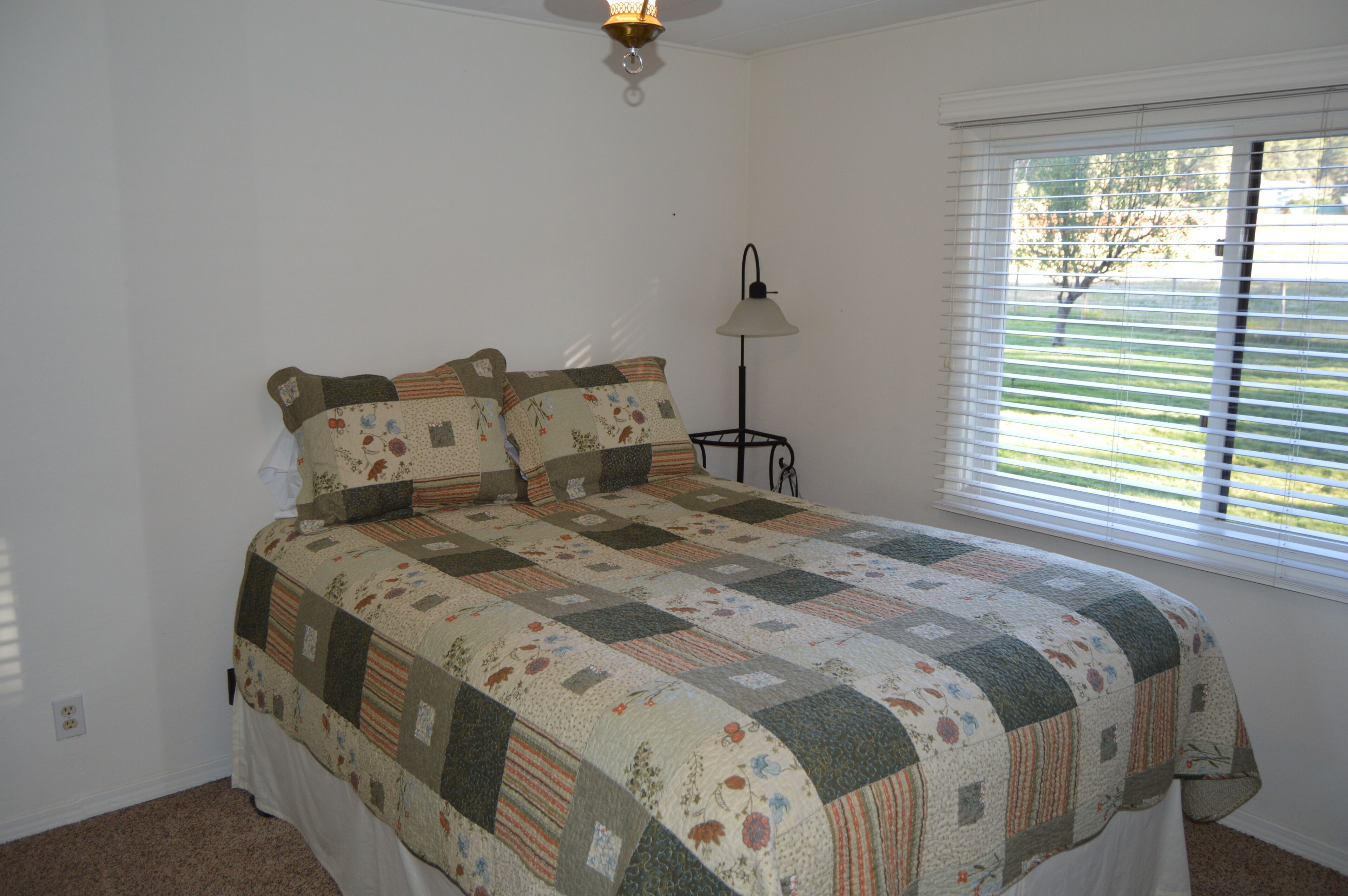 A bedroom with a bed, a nightstand, a lamp, and a window with blinds.