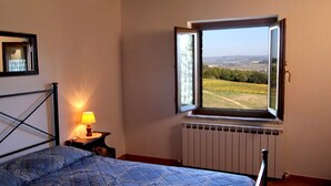 Une chambre à coucher avec un lit, une table de chevet avec une lampe, une fenêtre donnant sur un paysage et un radiateur.