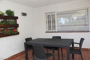 Un espace patio avec une table et des chaises, une fenêtre avec des stores et un jardinier mural agrémenté de plantes.